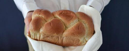 piekarz trzyma w dłoniach bochenek chleba